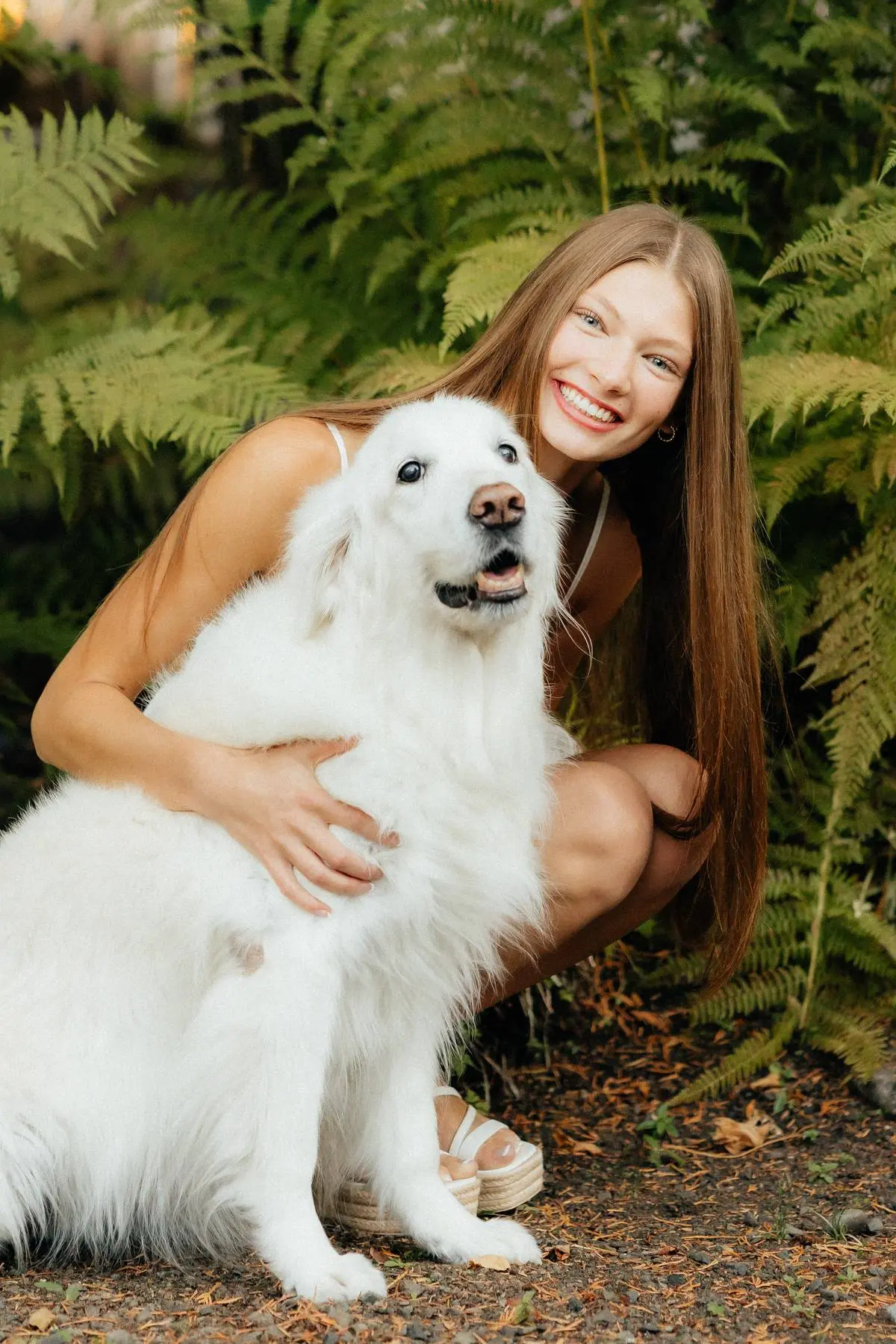 Madison hugging Lily, her white golden retriever, among ferns on Fox Island