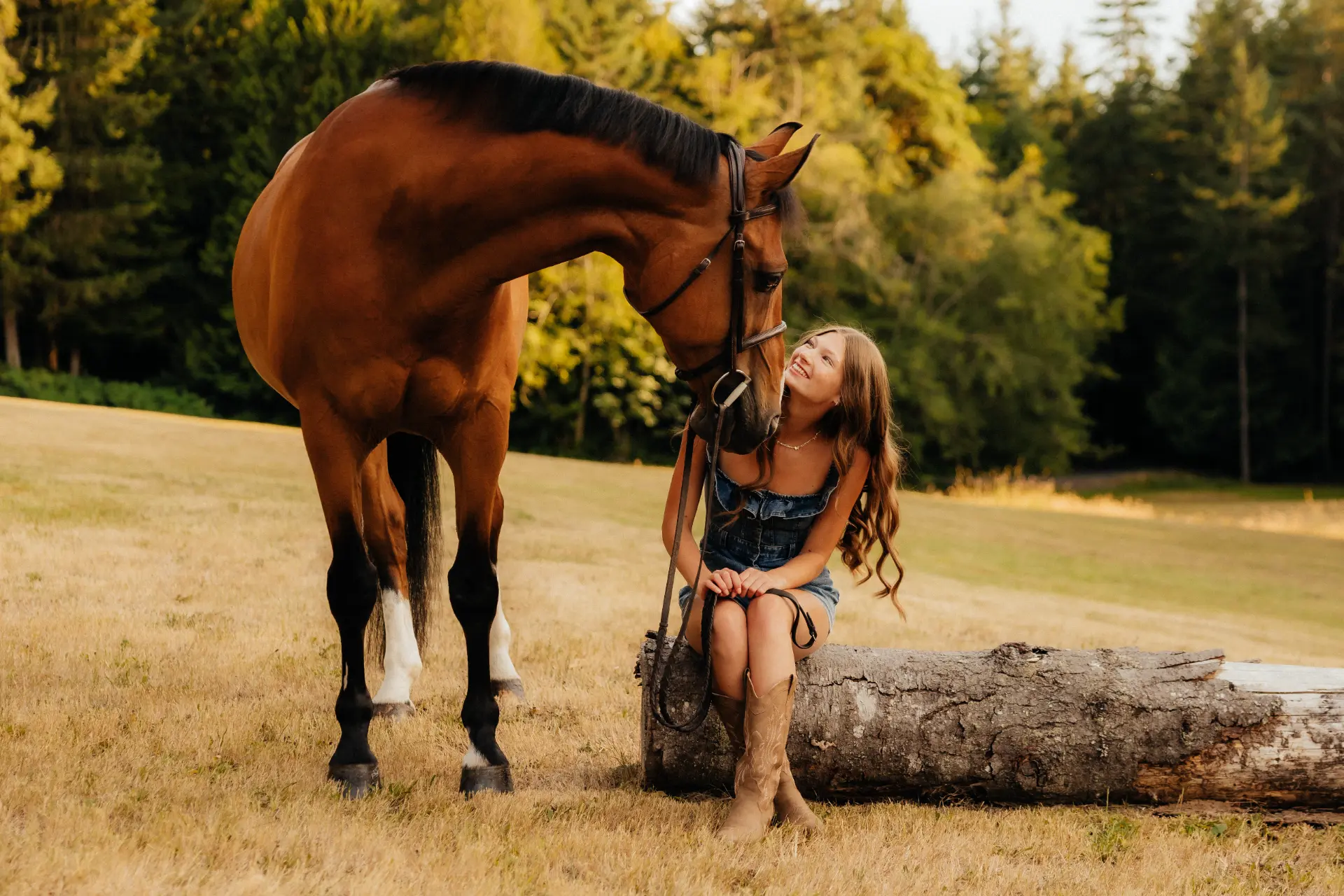 Madison seated on a log beside her bay horse in a sunny Gig Harbor field